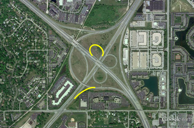 This figure shows an aerial photo of an interchange where drivers traveling northeast cannot enter the freeway traveling southeast without traveling completely through the interchange to make a U-turn. Drivers traveling northwest cannot access the route to the southwest without taking a circuitous path and backtracking.