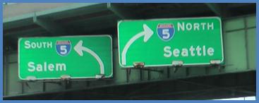 This photo shows guide signs associated with scenario 2 critical point 3. There are two green signs placed next to each other. The sign on the left has an arrow curving to the left and is labeled  5 South Salem.  The sign on the right has an arrow curving to the right and is labeled  5 North Seattle. 