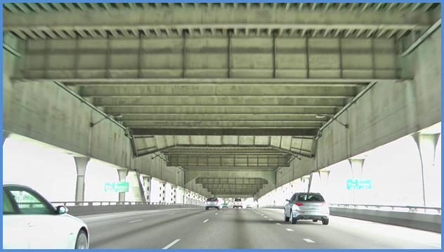 This photo shows the driving image for scenario 3 critical point 2. There is a four-lane single direction freeway with vehicles traveling on it. Two green signs are seen in the distance mounted to either side of the freeway.
