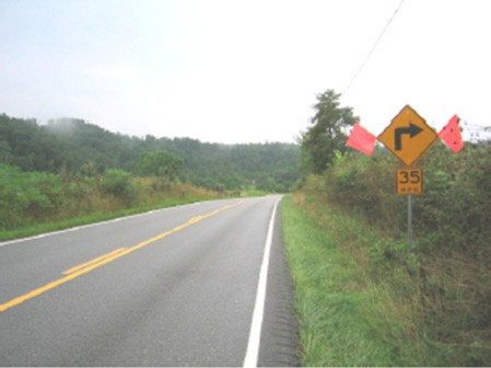 Figure 170. Photo. Flags to existing curve warning sign. This figure shows an example of red flags added to an existing curve warning sign. Red flags are added to an existing curve warning sign to attract driver attention.