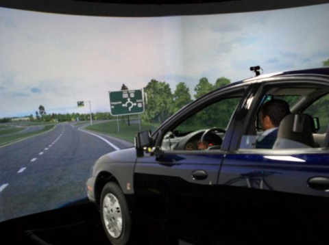 Figure 42. Photo. The FHWA Highway Driving Simulator. This figure shows the Federal Highway Administration Driving Simulator with a wraparound screen displaying a simulated view of the road in front of the test vehicle.
