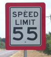 This is a photo of a white speed limit sign with black text and a red border. The sign reads as follows: 'SPEED LIMIT 55.'