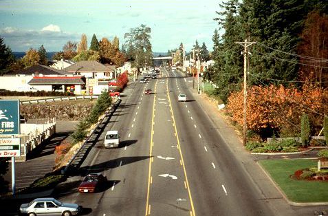 The picture is of a long, straight five lane road with a center turn lane. There are businesses along the road and traffic moves quickly. There is moderate traffic flow.