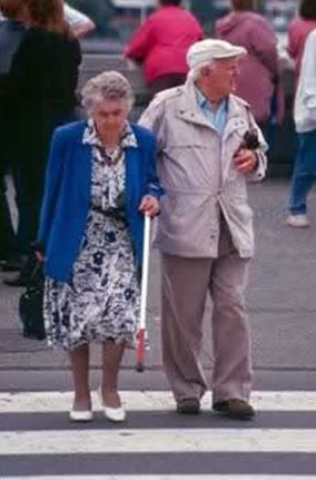 The picture shows an older man and woman pausing while crossing the street, apparently looking towards an approaching vehicle.