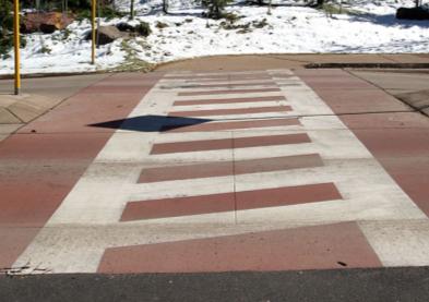 This photograph shows transverse with diagonal lines markings across a street as viewed from the curb. The markings consist of two thick, white horizontal strips with several thinner, diagonal lines connecting the two strips.