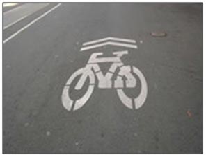 This photo shows an example of a shared lane marking, or sharrow. It consists of a bicycle outline underneath two chevrons.