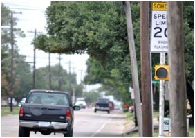 In this example of poor visibility, the driver's view of traffic control devices is obstructed by utility poles and trees. Only part of a school speed limit sign can be seen.