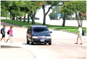 In this example of poor compliance, the driver is not yielding to pedestrians in the crosswalk. A minivan proceeds down the street with pedestrians attempting to cross the street on either side.
