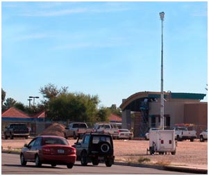 A temporary video trailer consisting of a base, a tall pole, and a camera is set up along a roadside to record traffic in the area of interest.