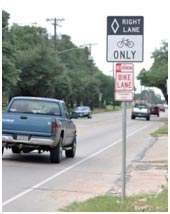 This photo shows a bike lane sign along the side of a two-lane road.