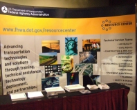 Photo of the FHWA Resource Center 10’ tall exhibit and a table full of materials in the exhibit hall of the Environmental Conference. 