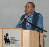 Caption: Photo of Mr. William Ambrose Littleghost, elder and cultural advisor, Sprit Lake Dakotah standing at a podium speaking and reflecting on the significance of the programmatic agreement. 