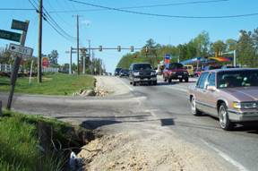 Photo of road showing cars driving next to a ditch on the shoulder of a road.