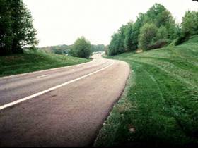 Scenic photo of grass on the side of a two lane road.