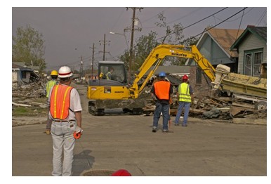Photo of workers surrounding a backhoe that is removing debris from storm damage on a residential street.