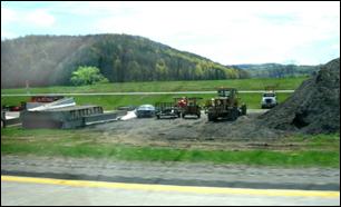 A storage area with a few supplies and construction equipment are shielded partially by a stock pile of excess fill.