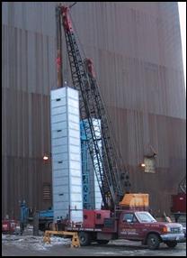 A 20 foot high, square dampener surrounds a pile driving hammer to minimize noise from the impact of the hammer on the pile.