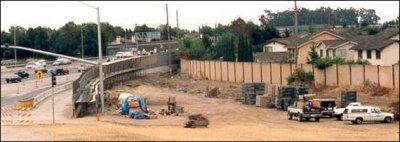 An existing noise barrier in between residences and highway widening construction is left in place until replacement barrier is constructed along highway right-of-way