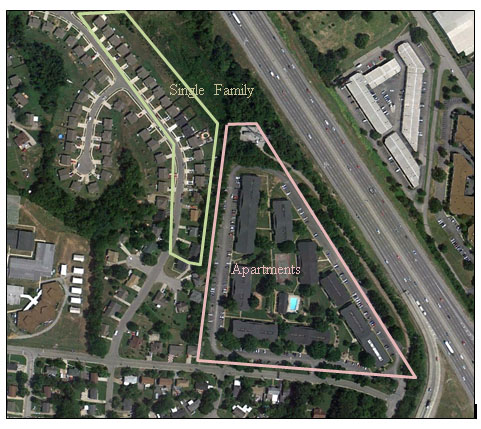 Aerial photo showing an apartment complex and a neighbrohood of single-family homes adjacent to an eight-lane interstate. 