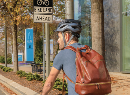 Image shows man on bicycle in a bike lane with his helmet and backpack on, as if he is riding his bike to school or work.