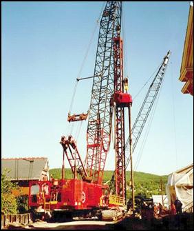 A crane with pile driving hammer with a nearby residence in the background. Pile driving is an extremely noisy activity.