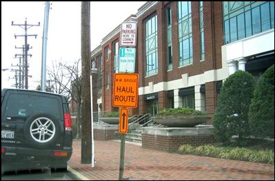 An orange sign with directional arrow posted on existing sign pole designating a street as a haul route for trucks on the Woodrow Wilson Bridge project in metro DC area. 