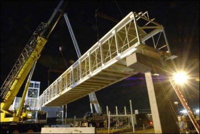 A crane is placing a span of bridge onto two abutments on a nighttime bridge project.