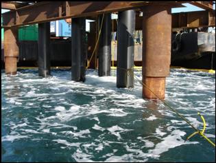 A bubble curtain operates around an underwater pile that is part of a multiple pile structure. The air bubbles are visible at the water surface.