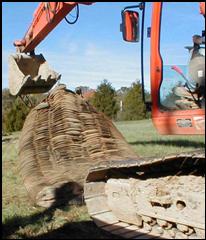 A blasting mat made of black tires is being placed into position with a excavator.