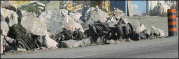 Blasting mats constructed with black tires can be seen intermingled amongst a pile of large rocks post blast.