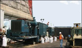 Several construction workers and stationary and mobile equipment can be seen working within the enclosed site.