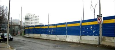 A temporary barrier combination of a panel of plastic material mounted on a portable jersey barrier block a construction site from an adjacent roadway in an urban area.