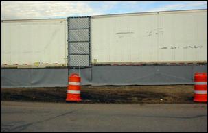 A close-up of the vinyl sheeting extending from the back and bottom of the tractor trailers which fills in the gaps left between and underneath the trailers to completely block the line-of-sight from the construction site to the receivers.