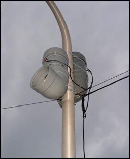 Close-up of experimental sound system mounted on the light pole at right angles in direction of nearby residences. Speakers and amplifiers consist of elbows of wide plastic pipe where the top is enclosed to weather and the side is open to permit transmission of sound from speaker.