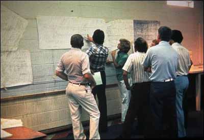 Several concerned citizens view project plans posted on display in the front of a classroom.