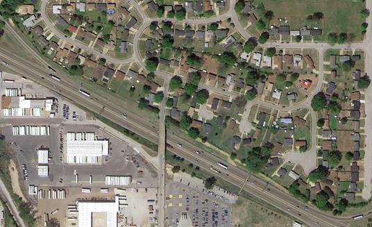 Aerial photo showing community for which a noise barrier was proposed by TDOT, Project TDOT-4. It shows single family houses that are owner-occupied. The barrier was determined to be reasonable due to unanimous support for the barrier. The roadway curves from the upper left to lower right corners. The residential land uses are above the road and commerical land uses below the road. 
