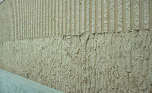 Photo of the highway side of a noise barrier with contrasting textures. A rough texture on the bottom of the barrier and a vertical groove texture is on the top