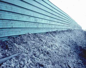 Photo of snow stored at the base of a noise barrier adjacent to the highway