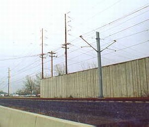 Photo showing the top of a noise barrier and overhead power lines.