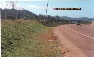 photo:  earth berm, with trees planted on the top of the berm, and a highway with traffic (photo is intended to illustrate a typical example of an earth berm-type noise barrier)