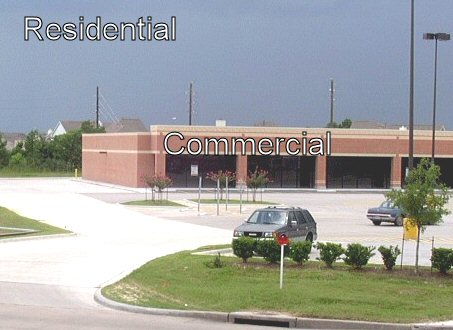 A commercial land use with a large parking lot is located between a roadway and a residential land use.