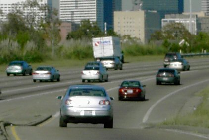 This slide shows several automobiles entering a multi-lane roadway via an on-ramp. There are several vehicle types on the roadway and urban development in the background.