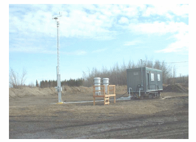  A photograph of an example monitoring station. The photograph shows an instrument trailer positioned in a remote field with a 10 meter meteorological tower and two PM10 samplers located near the monitoring station.