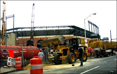 Several pieces of construction equipment, including a front-end loader, are working near a sports stadium.