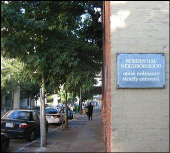 A sign on a building in an urban setting stating this residential neighborhood strictly enforces its noise ordinance.