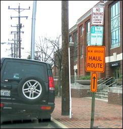 An orange sign with directional arrow posted on existing sign pole designating a street as a haul route for trucks on the Woodrow Wilson Bridge project in metro DC area. 