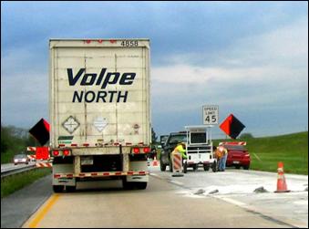 A heavy truck passes by a construction zone in the left lane while the right lane pavement is under rehabilitation.