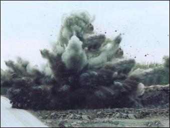 An explosion with smoke and debris flying from a blasting operation near a low volume roadway; blasting is an extremely noisy activity. 