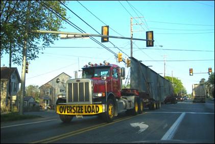 A heavy truck designed for oversized loads transports long and wide steel beams on a residential road.