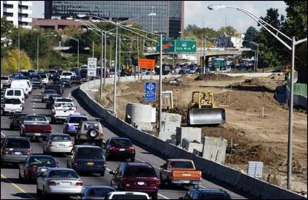 A highway separated by a jersey barrier from an adjacent highway widening project is congested with the traffic diverted because of the project.